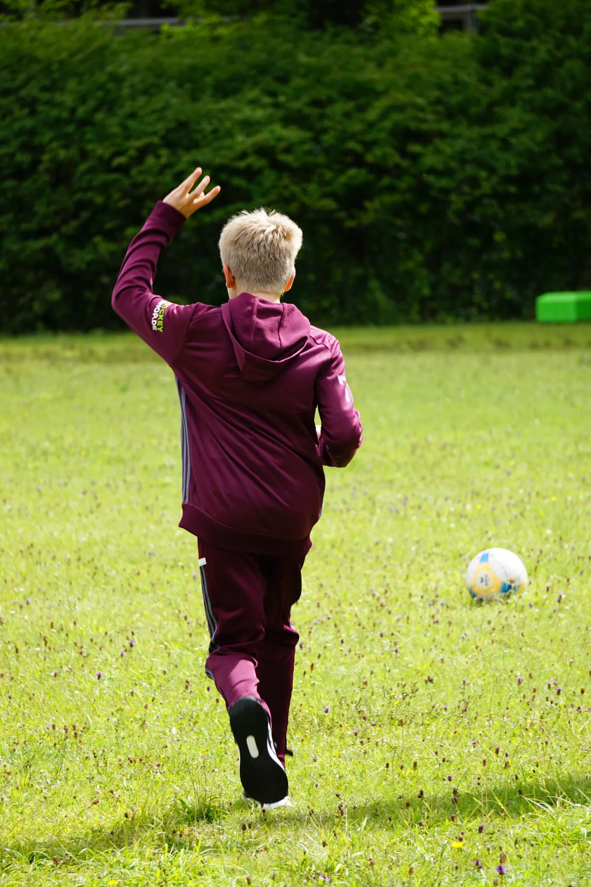 Junge von hinten rennt auf Fu&szlig;ballfeld dem Ball hinterher