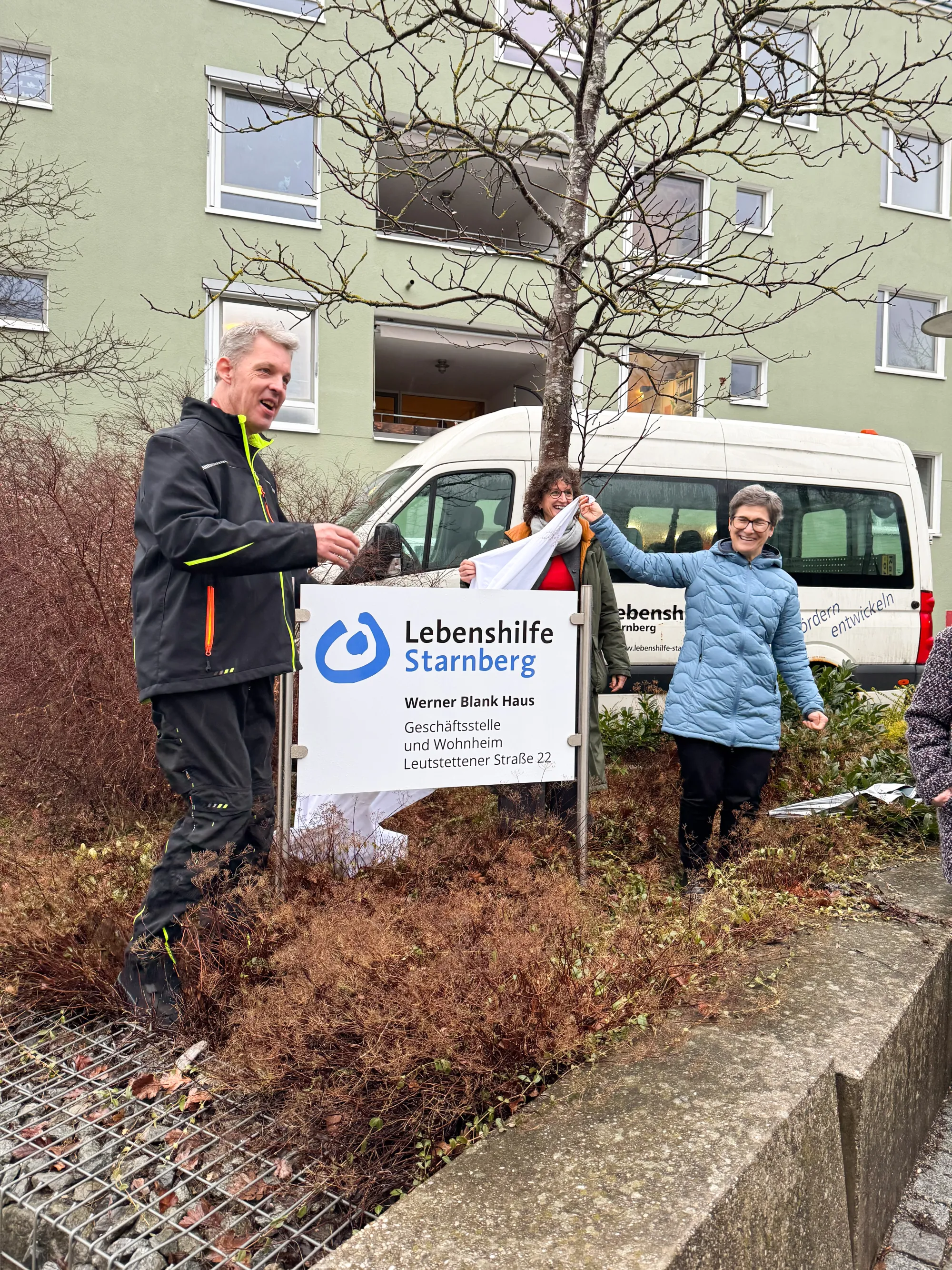 Die Gesch&auml;ftsf&uuml;hrerin, die Vorstandsvorsitzende und ein Bewohner enth&uuml;llen das neue Schild mit der Aufschrift "Werner Blank Haus", indem sie ein Tuch vom Schild ziehen.
