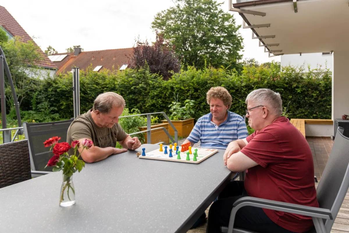 Drei Männer spielen auf dem Gartentisch "Mensch ärgere dich nicht"