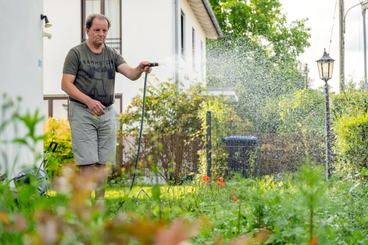 Älterer Mann gießt den Garten mit einem Gartenschlauch