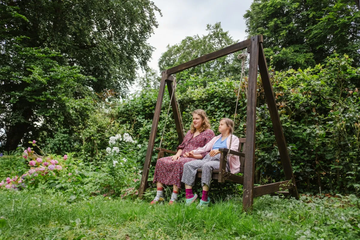 Zwei Frauen sitzen auf einer Hollywood-Schaukel im Garten