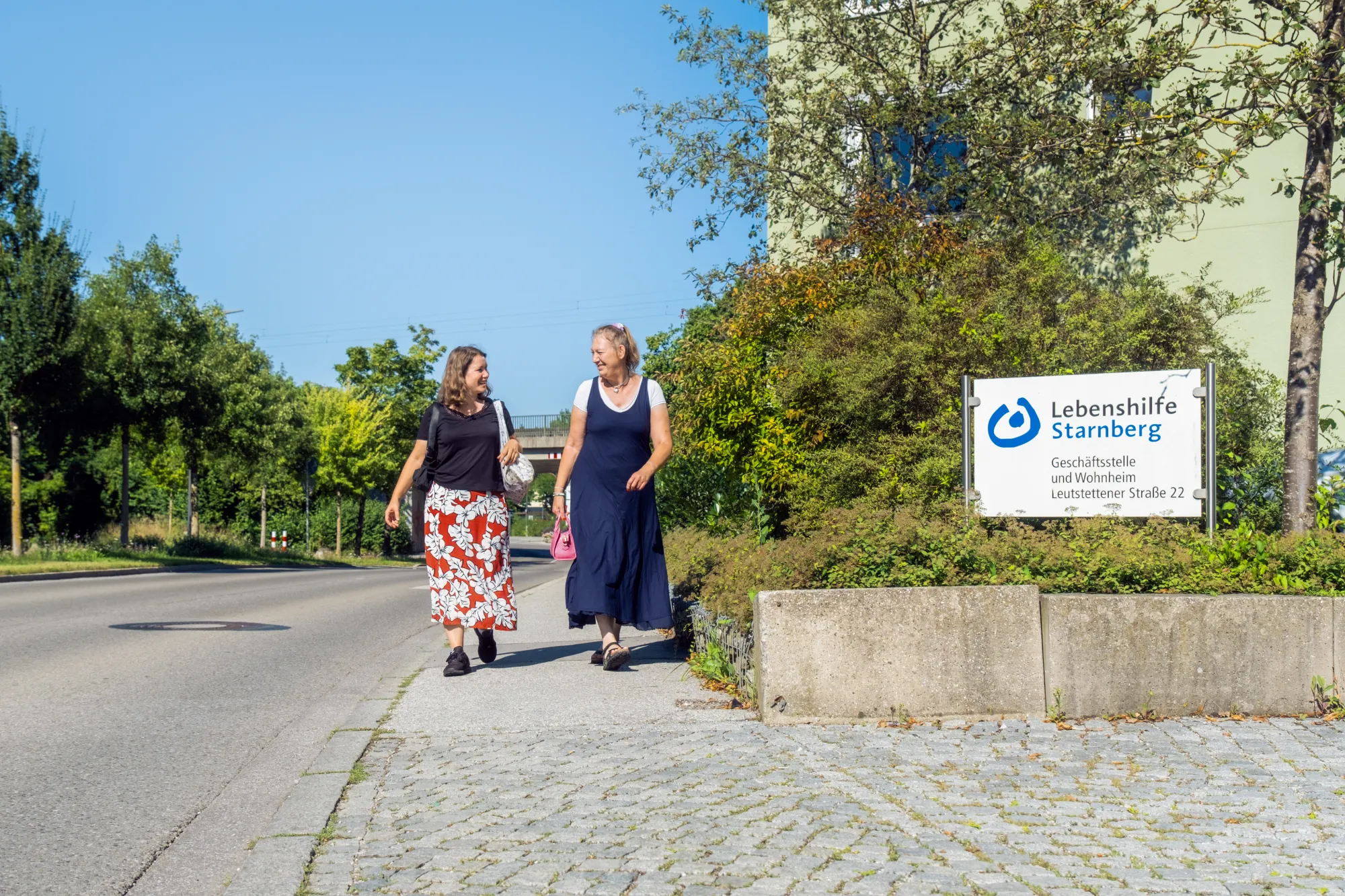 Frau mit Behinderung und Betreuerin gehen auf Gehsteig vom Einkaufen nach Hause
