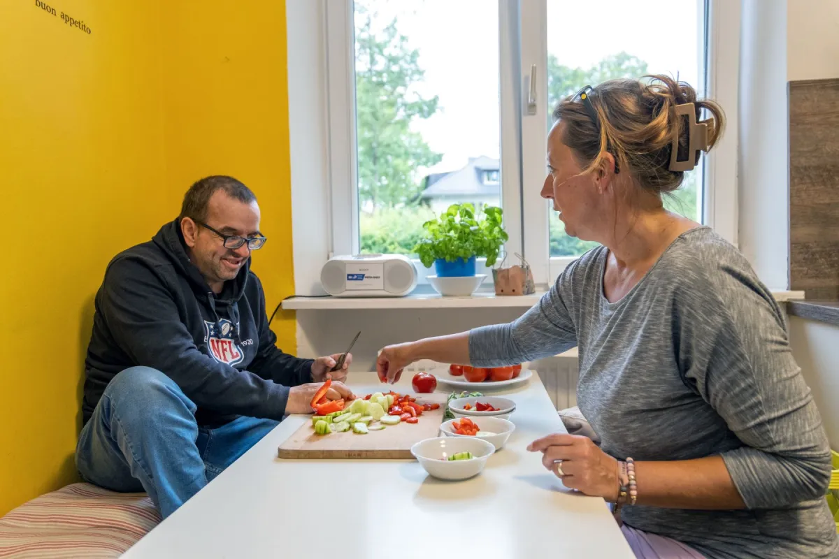 Betreuerin hilft Mann beim Schneiden von Gurke und Paprika