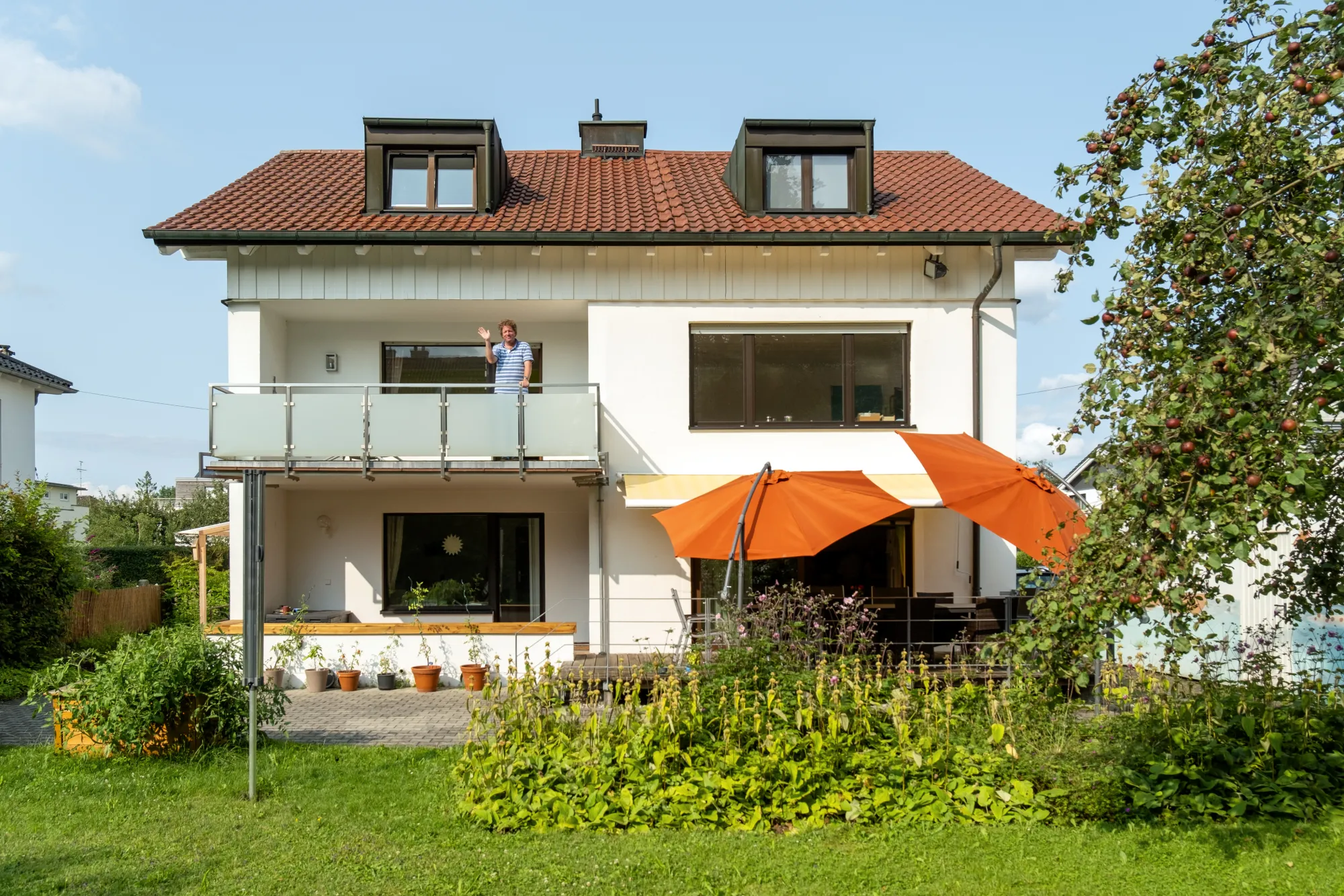 Dreist&ouml;ckiges Wohnhaus, Mann winkt vom Balkon runter