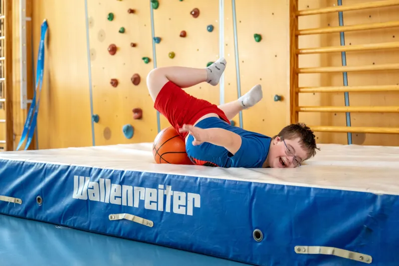 Kind turnt vor einer Kletterwand in der Turnhalle