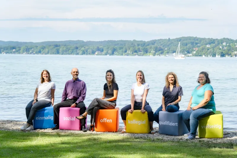 Gruppe von Menschen sitzt mit bunten W&uuml;rfeln am Ufer des Starnberger Sees